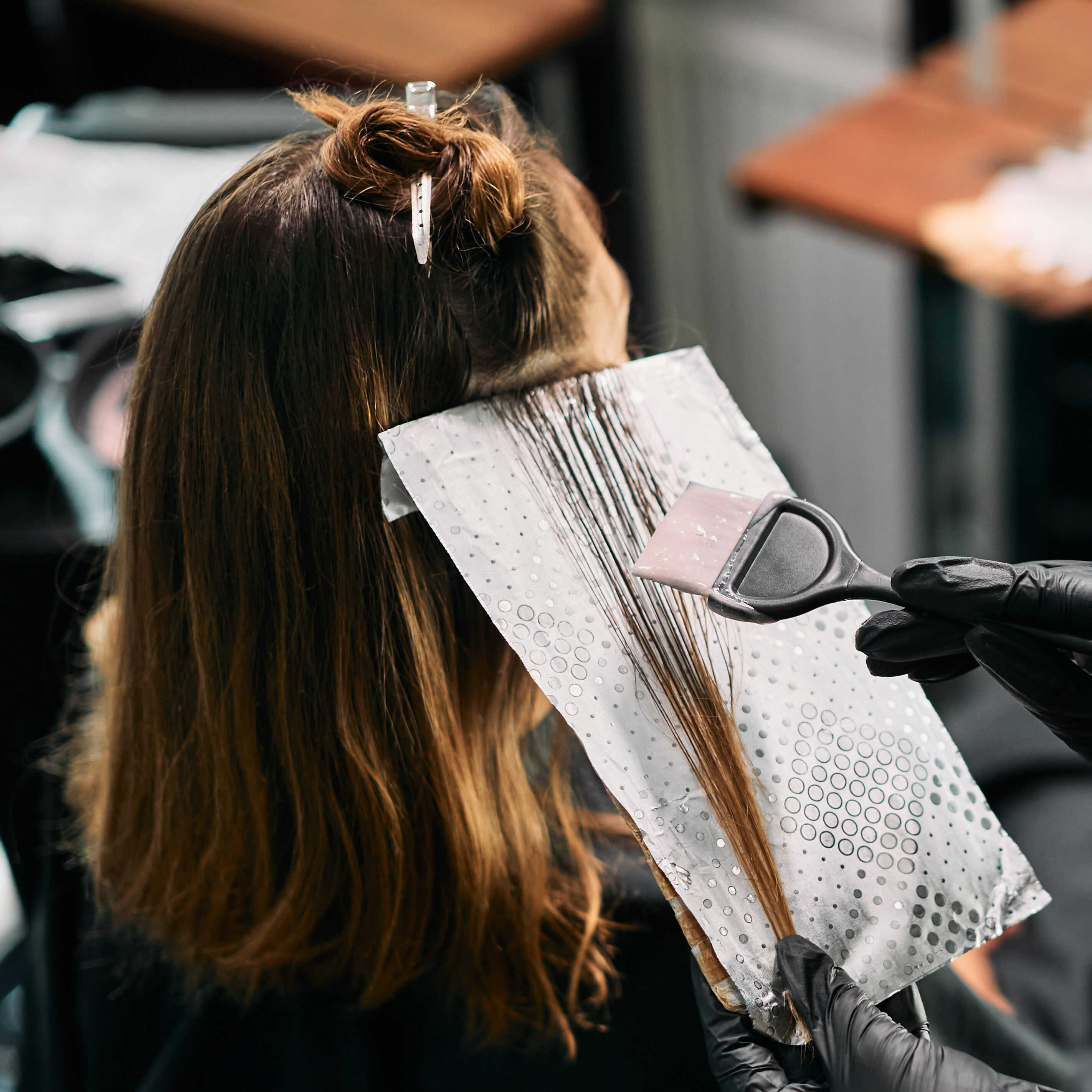 Close-up of hairdresser dyeing customer's hair at the salon.