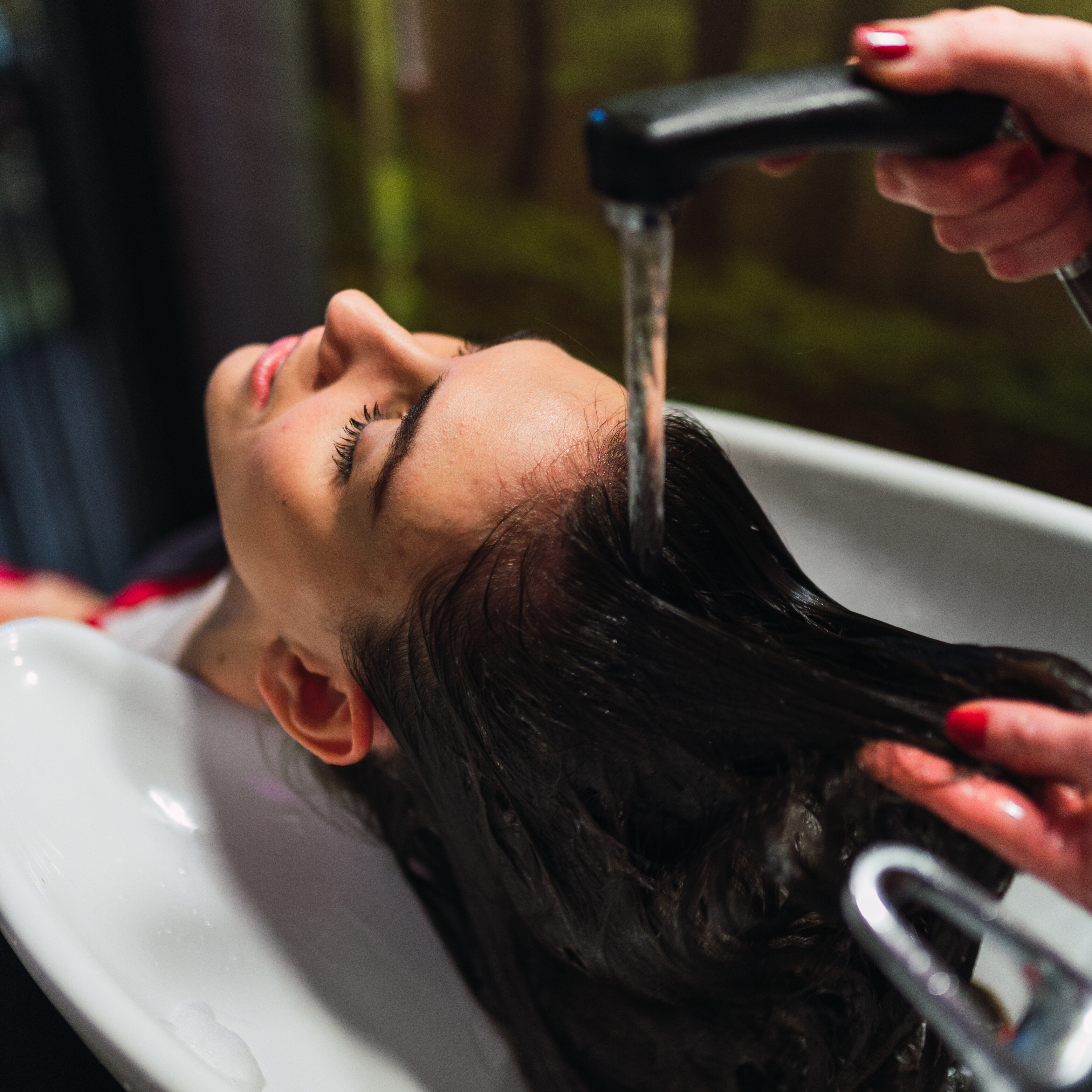 Stylist washing hairs to young lady